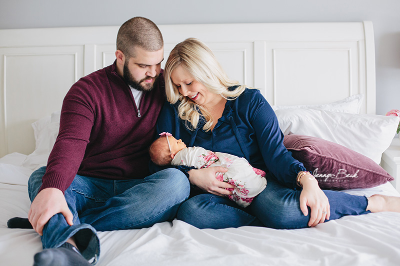 westerville ohio newborn photographer - mom and dad sitting on bed smiling down on new baby girl