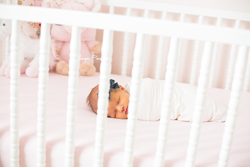baby girl swaddled in white sleeping in crib with blue velvet bow