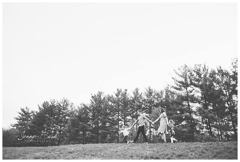 family walking down hill holding hands with evergreen trees behind