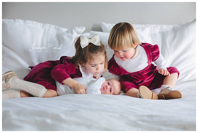 two young girls sitting on parents bed looking down at new baby sister