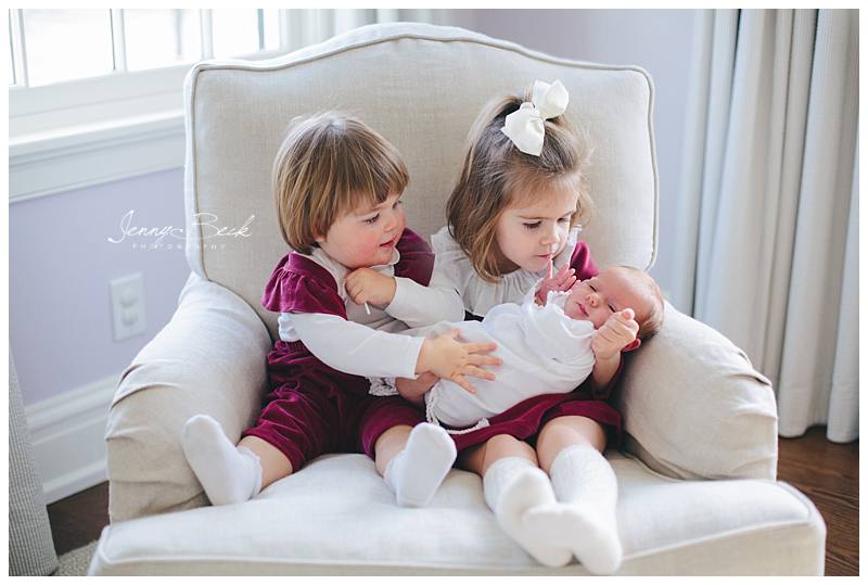 two big sisters holding new baby sister in classic rocking chair