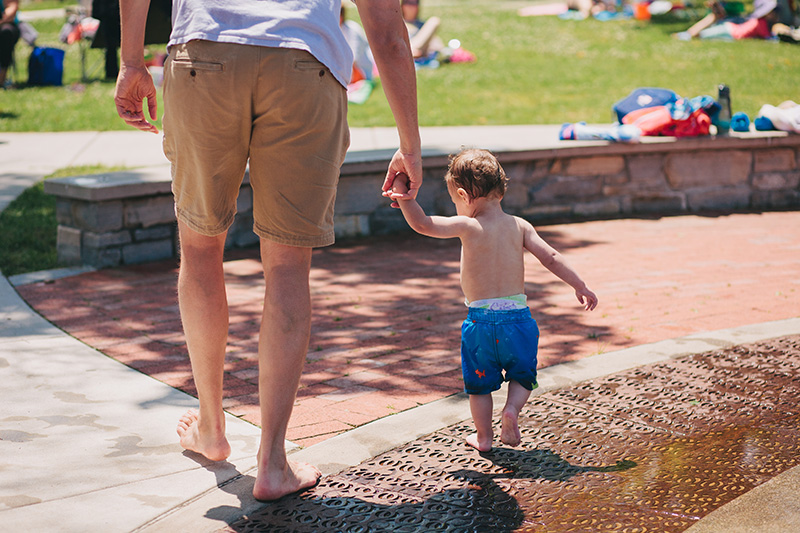 dad holding young boy's hand a the splash park in traverse city
