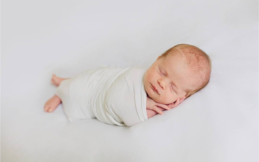 newborn posed on white backdrop wrapped in simple white wrap
