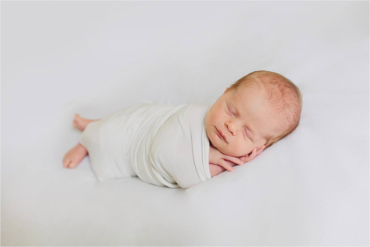 newborn posed on white backdrop wrapped in simple white wrap