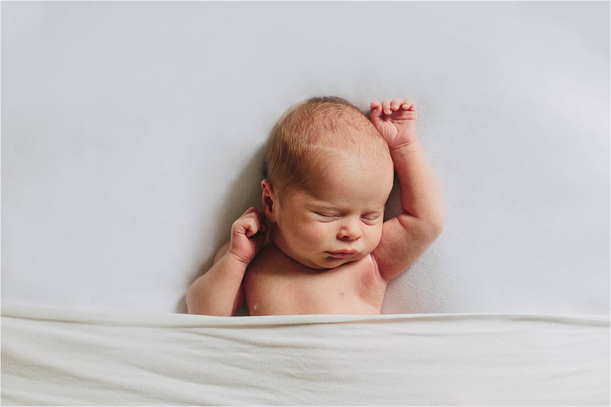 baby lying on back with arms up naturally with white minimal backdrop